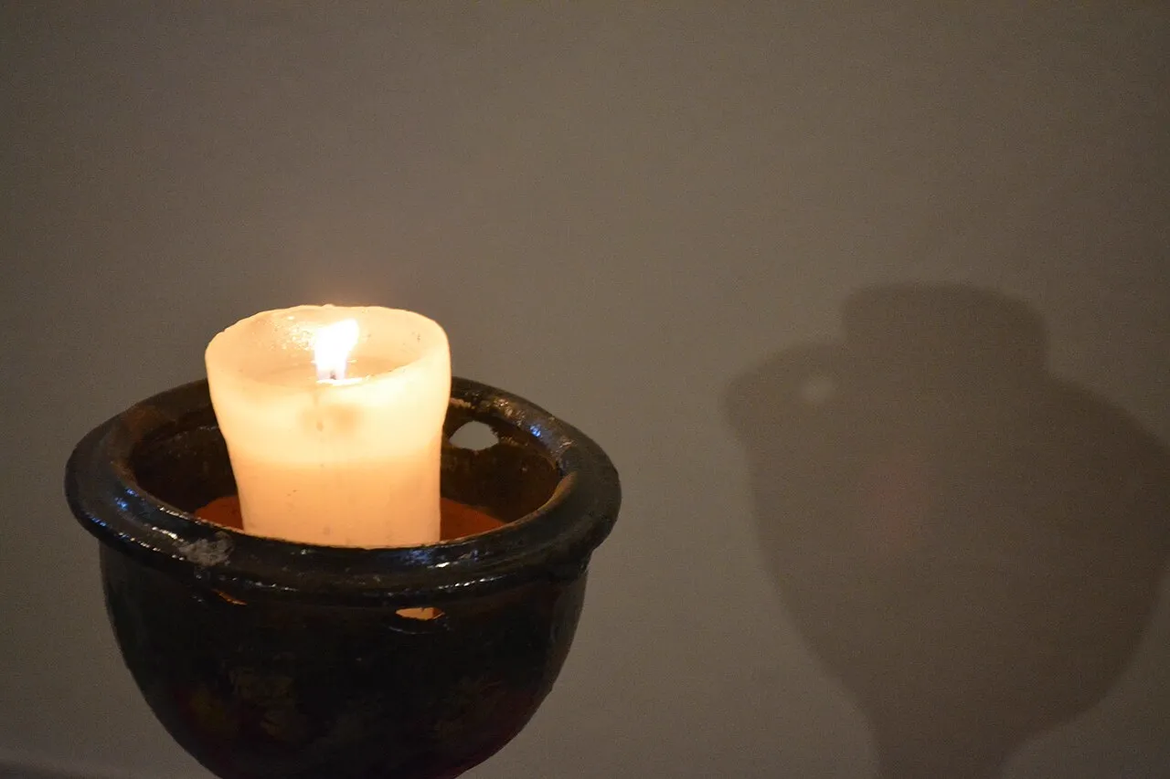Candela bianca accesa in un recipiente di terracotta scura