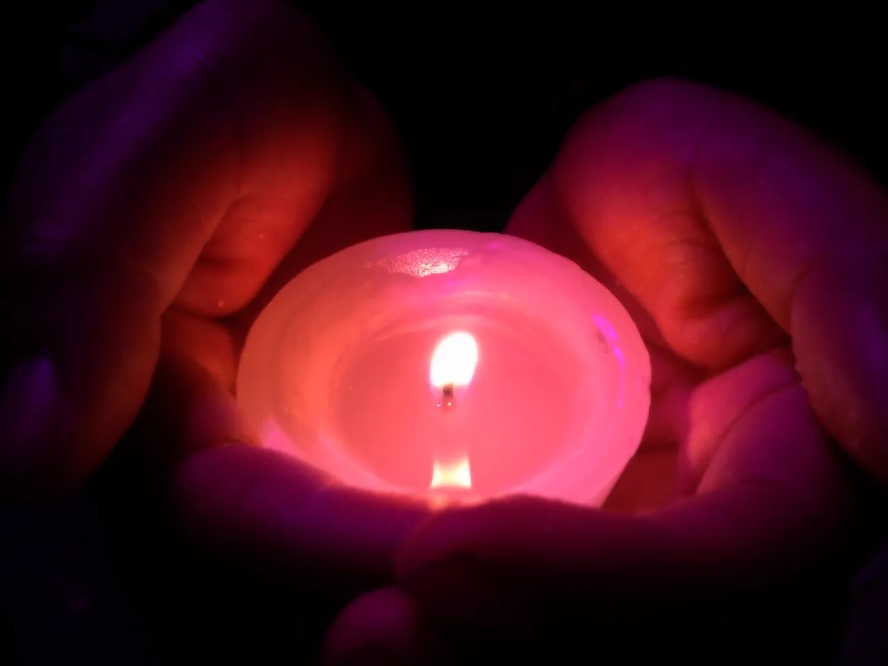 Mani che custodiscono una candela rossa accesa nel buio